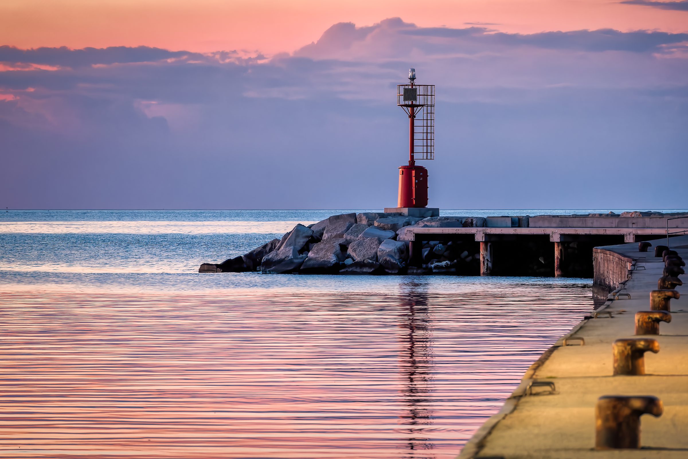 Tranquil Adriatic dawn with pink and purple sky over Gabicce Mare harbor with red beacon at pier