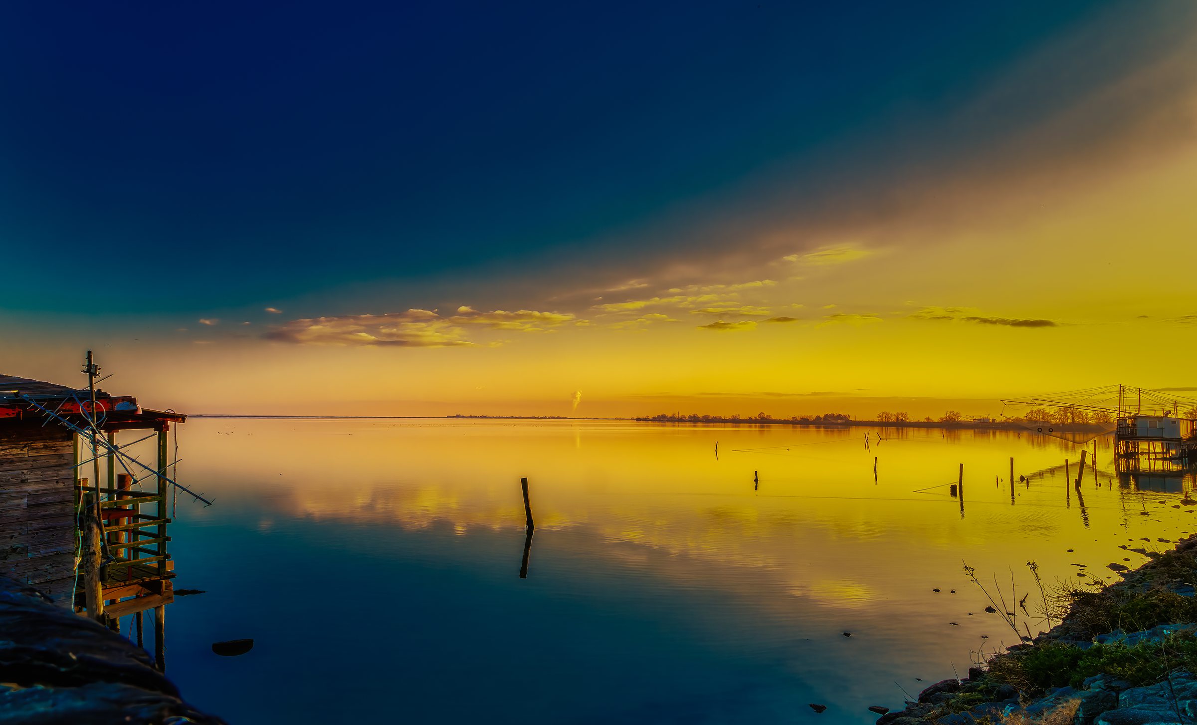 Sunset Magic: Driving Through the Valli di Comacchio Wetlands 7 Dawn gradient from deep blue to golden amber over Valli di Comacchio fishing structures