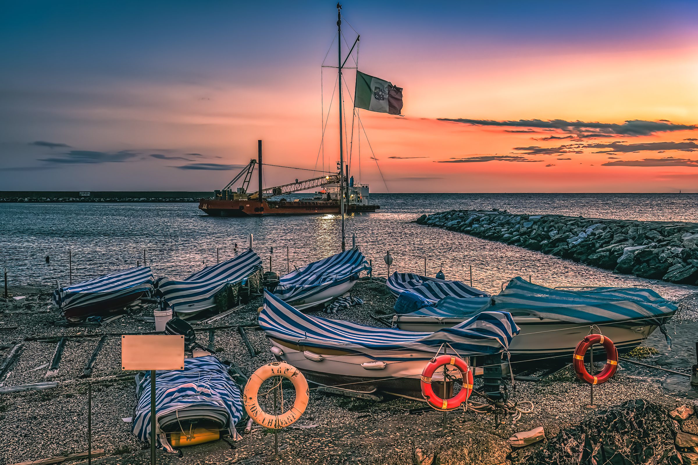 Twilight scene in Chiavari with striped fishing boats on shore under vibrant sunset sky